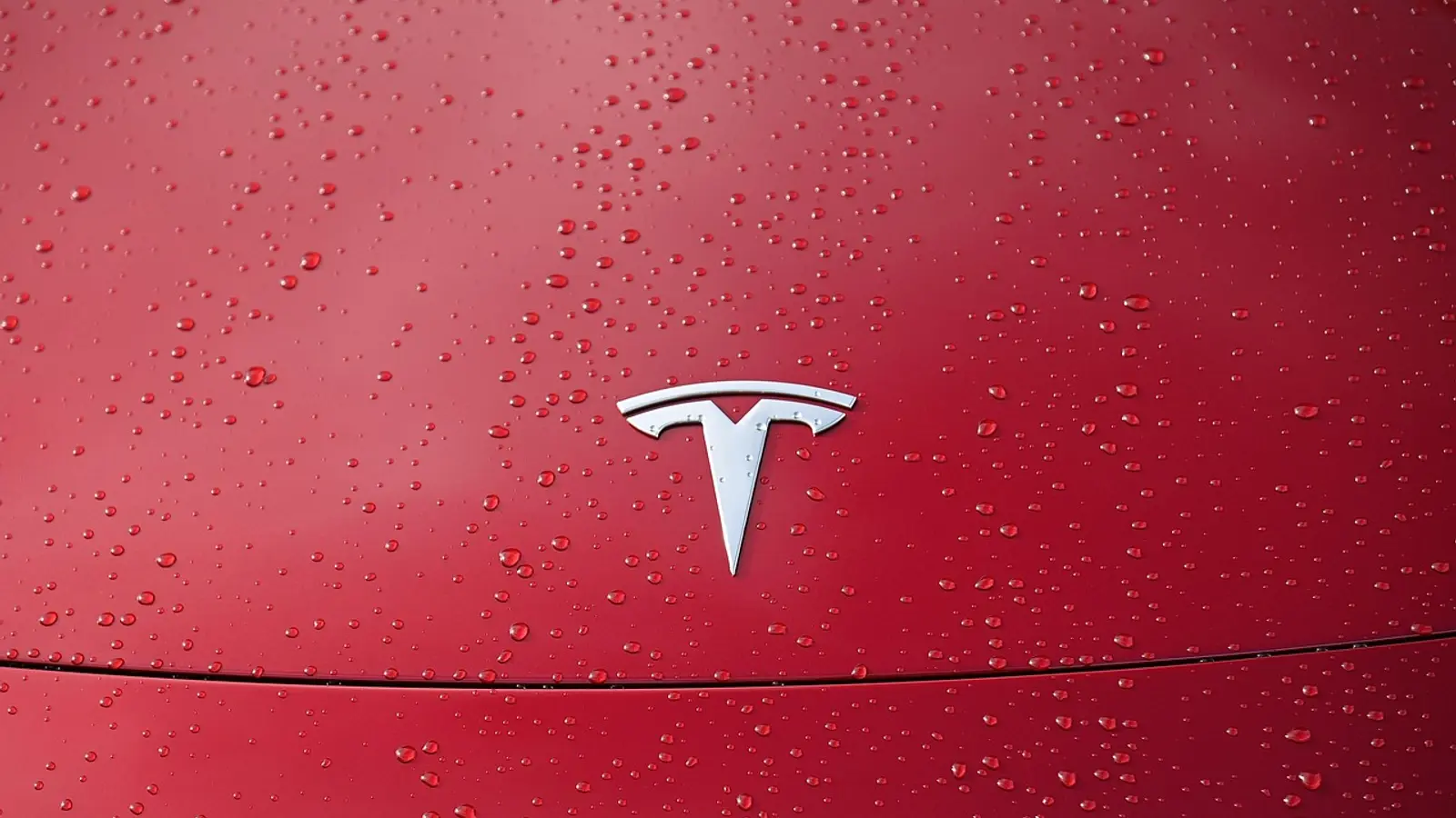 Logotipo da Tesla no capô de um carro vermelho coberto de gotas de chuva